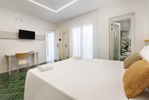 Habitación de hotel con cama, escritorio, silla, televisor y baño visible a través de una puerta abierta.