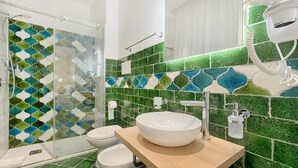 Un baño con cabina de ducha de vidrio, un lavabo blanco y un secador de pelo en la pared.