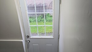 Eine weiße Tür mit Fenster, Holzdielen und einem Metallgeländer.