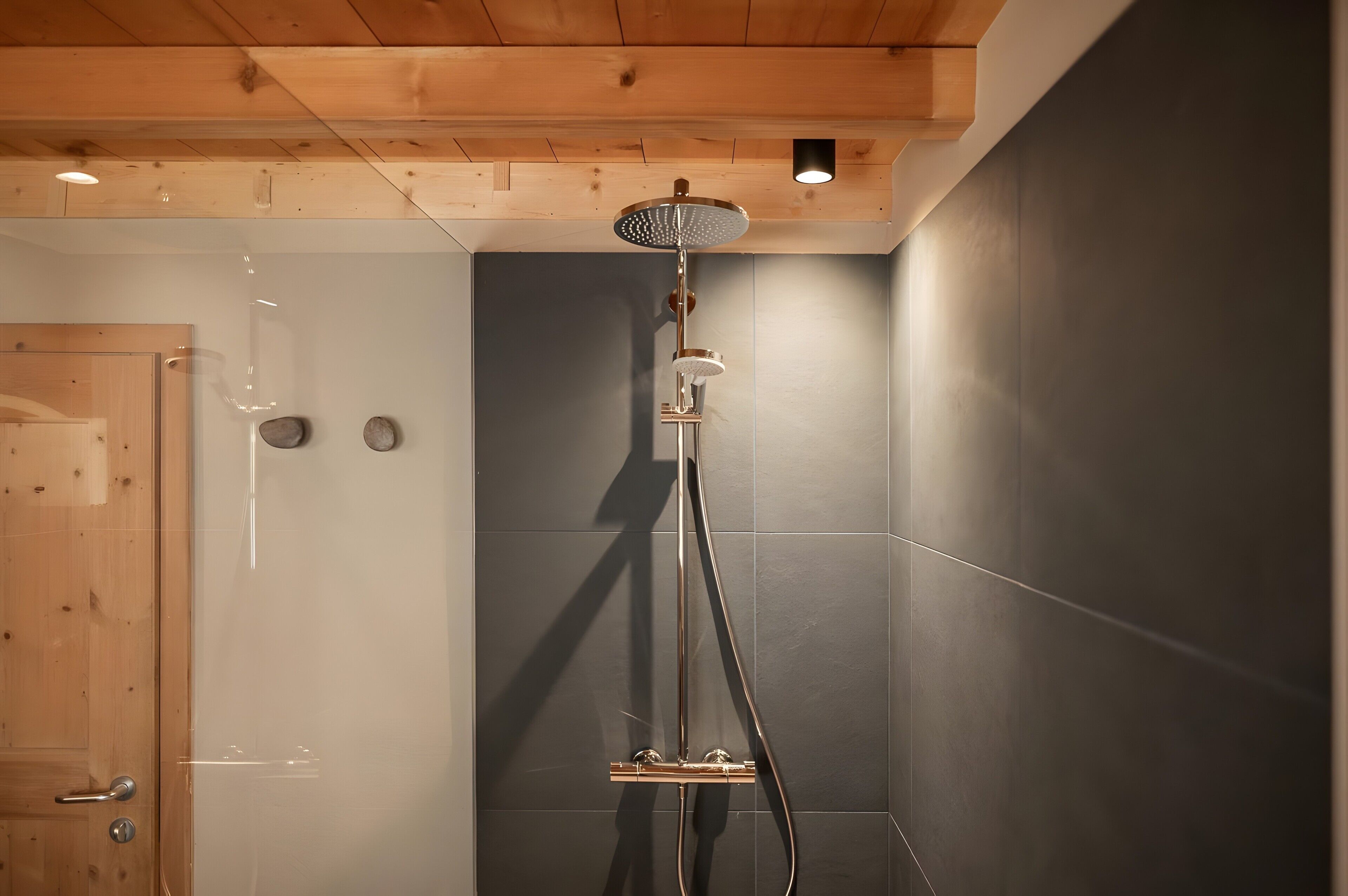 A shower with a handheld head, a wall-mounted control panel, and a wooden ceiling.