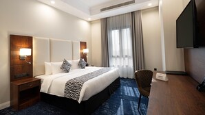 Une chambre d’hôtel avec un grand lit, un bureau, une chaise, une télévision et une fenêtre avec des rideaux.