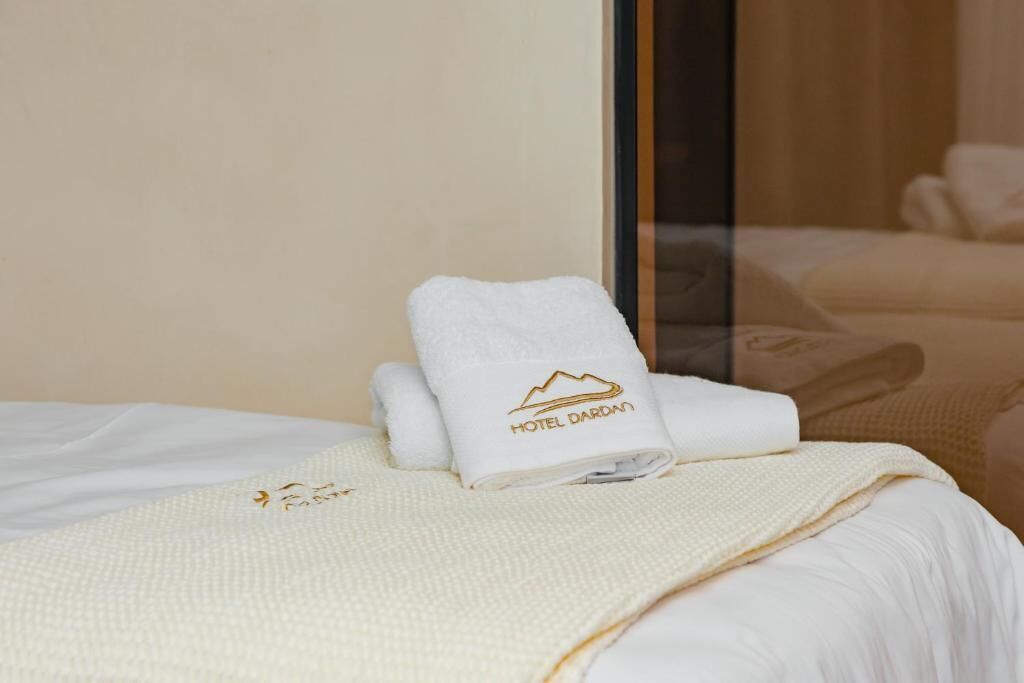 Una cama bien hecha con una manta blanca y una toalla con el logotipo del hotel.