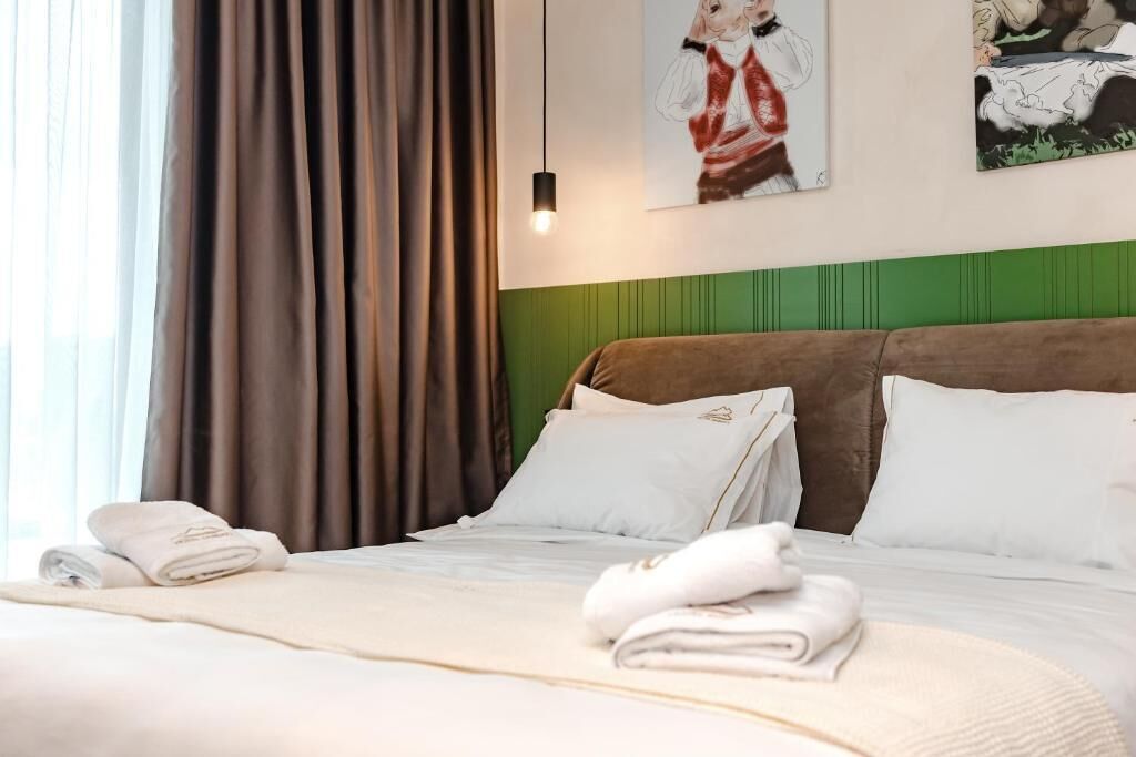 A hotel room with a bed, pillows, a blanket, and a painting on the wall.