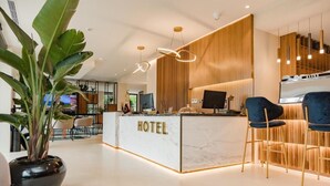 Un área de recepción de hotel moderna con mostrador de mármol, paneles de madera y una planta en maceta.