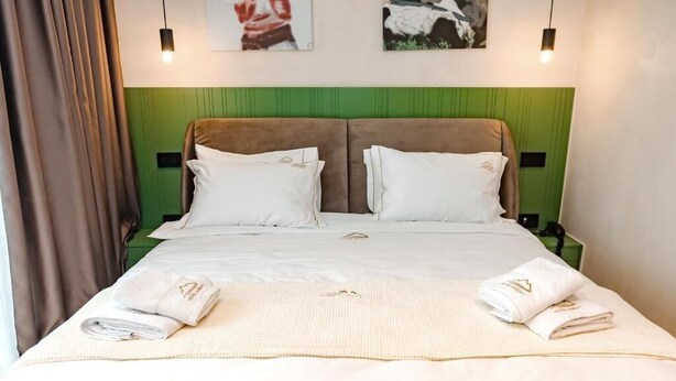Una cama doble con cabecera verde, ropa de cama blanca y dos mesitas de noche con lámparas.
