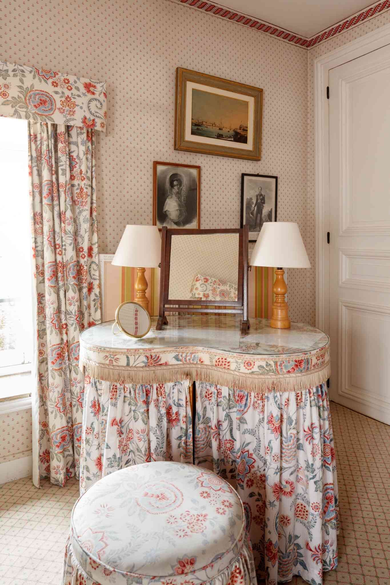 A room with a round table, two lamps, a mirror, and a framed picture on the wall.