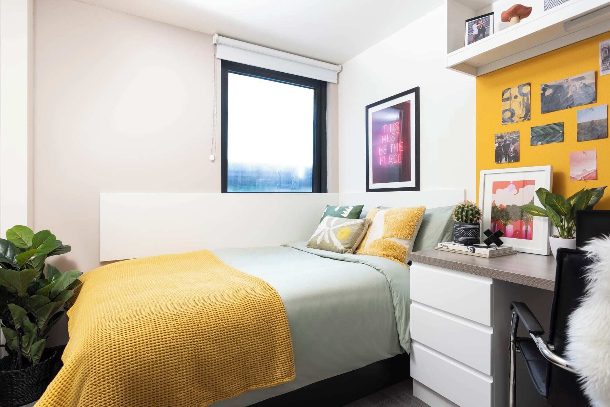A bedroom with a bed, a desk, a window, and wall decorations.