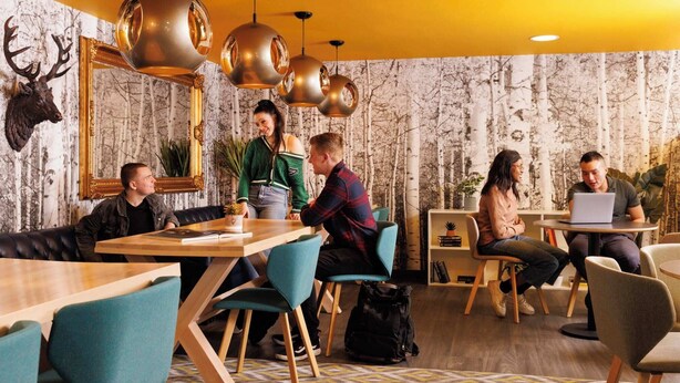 A modern interior with wooden tables, teal chairs, and a forest-themed wallpaper. - Student Only Brass Founders (Sheffield)