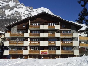 Ein mehrstöckiges Hotel mit Balkonen, einer Schautafel und einer Bergkulisse.