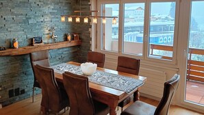 A dining area with a wooden table, chairs, a decorative bowl, and a stone wall. - Frégate 44 # 4-bed apartment, Dusche, WC 4-Bettwohnung, Dusche, WC by Interhome (Leukerbad)