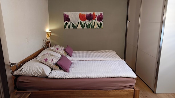 A bedroom with a wooden bed, a wall-mounted lamp, and a painting of tulips. - Frégate 44 # 4-bed apartment, Dusche, WC 4-Bettwohnung, Dusche, WC by Interhome (Leukerbad)