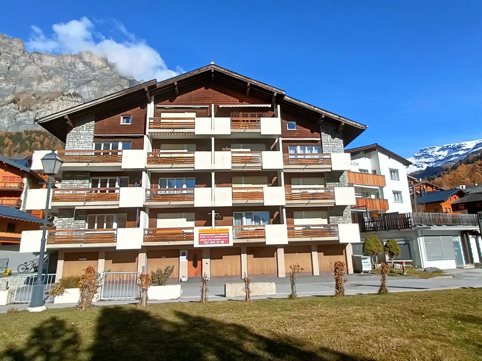 Un immeuble à plusieurs étages doté de balcons, d’une enseigne et ayant une chaîne de montagnes en arrière-plan.