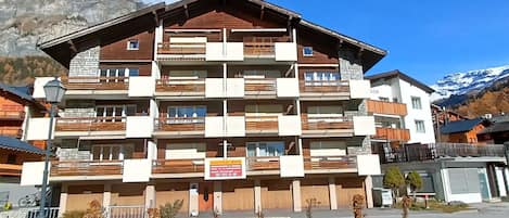 Un immeuble à plusieurs étages doté de balcons, d’une enseigne et ayant une chaîne de montagnes en arrière-plan.