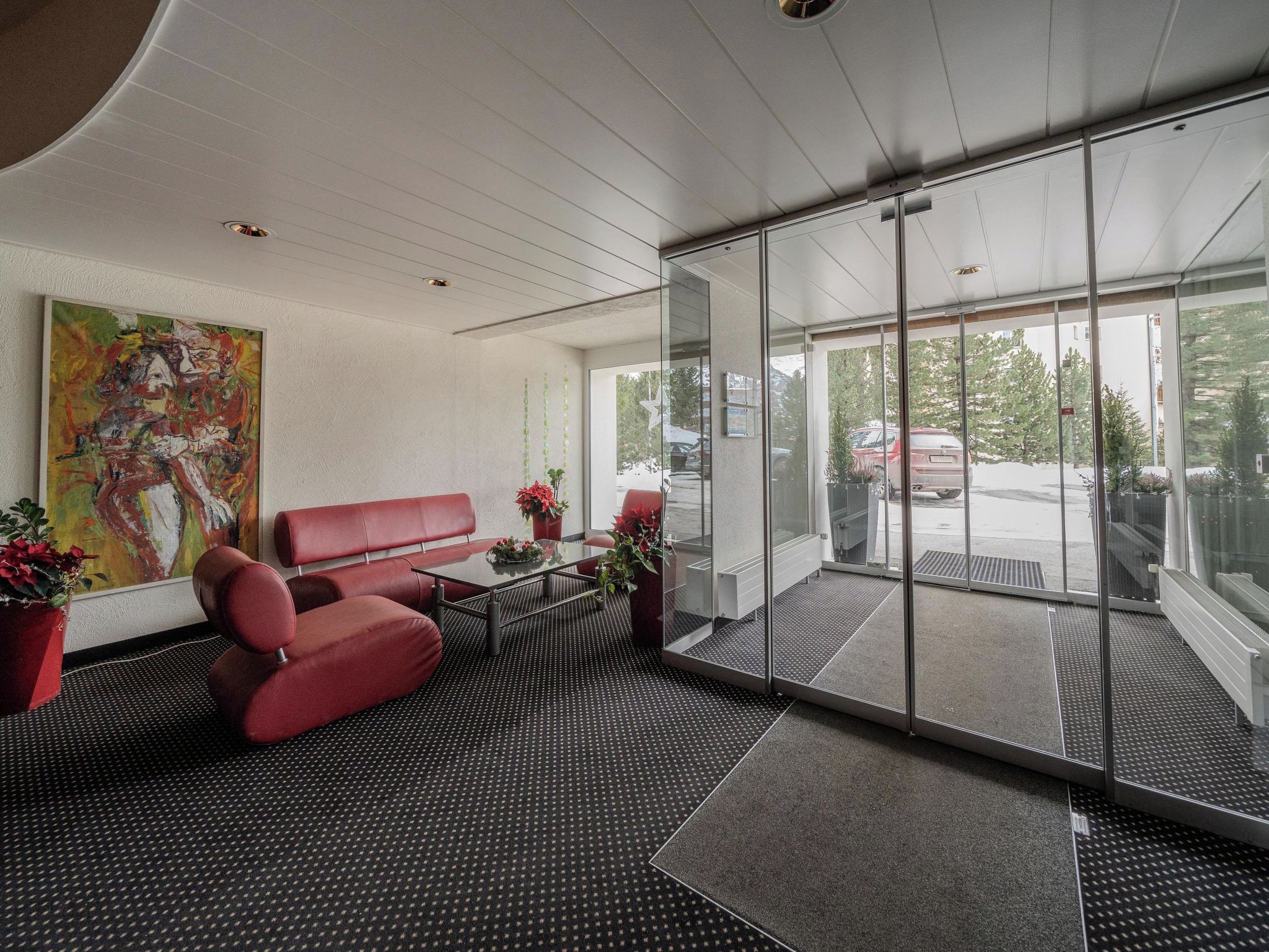 Un área de espera moderna con un sofá rojo, una pared de vidrio y vista al estacionamiento.