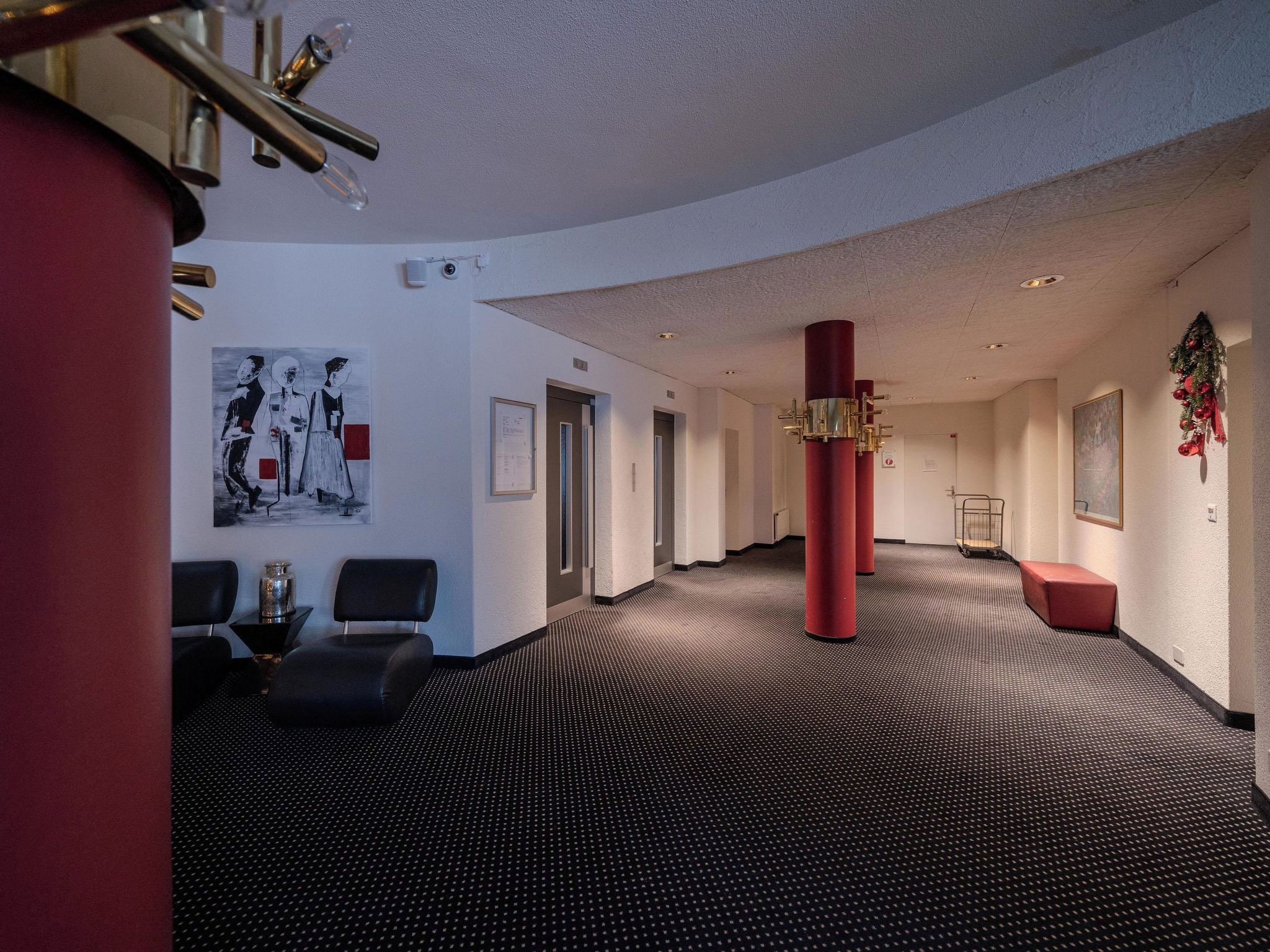 A hotel lobby with a black and white patterned carpet, red pillars, and a framed artwork on the wall.