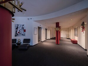 Eine Hotelhalle mit einem schwarz-weißen Teppichmuster, roten Säulen und einem gerahmten Kunstwerk an der Wand.