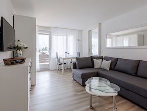 Ein modernes Wohnzimmer mit einer Couch, einem Glastisch und einem Essbereich mit Tisch und Stühlen.