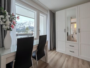 Ein Zimmer mit Schreibtisch, zwei Stühlen, einem großen Kleiderschrank, einem Spiegel und Bergblick.