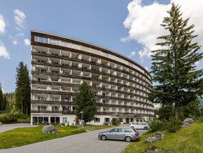 Ein mehrstöckiges Hotel mit geschwungener Fassade, Balkonen und einem Parkplatz mit Autos.