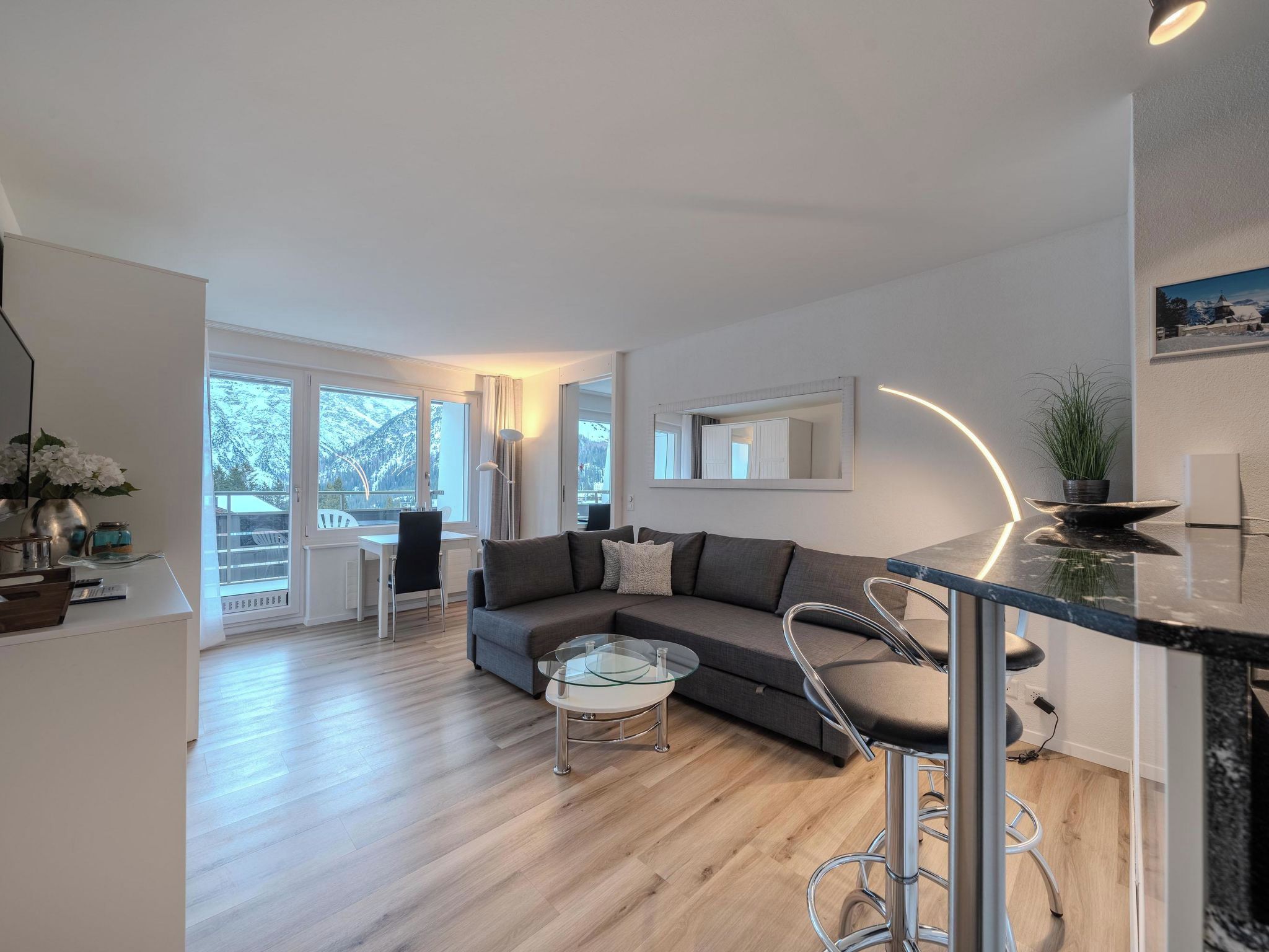 A modern living room with a sofa, a glass coffee table, and a dining area with a bar.