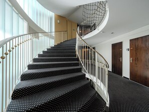Eine Wendeltreppe mit schwarzen Stufen und weißen Spindeln, die zu einer Zwischenebene mit einer Glaswand und einer Holztür führt.