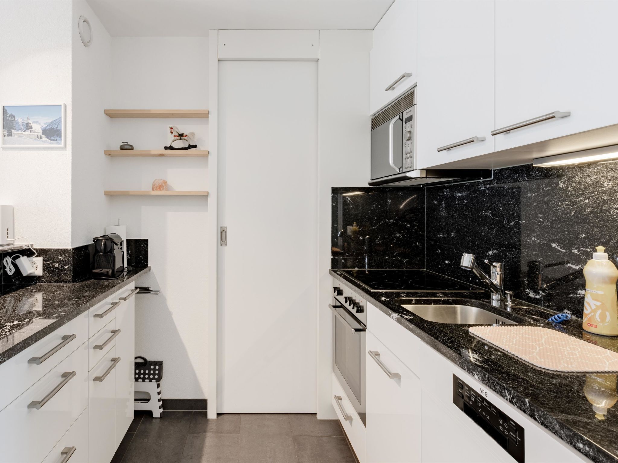A modern kitchen with black countertops, white cabinets, and a stainless steel sink.