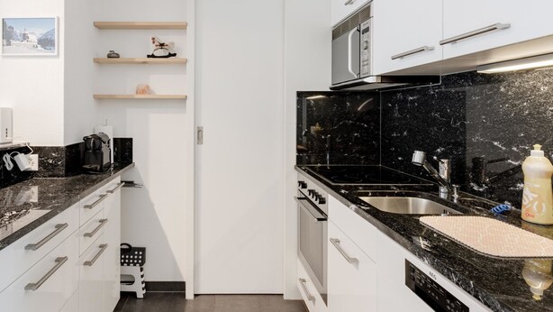 A modern kitchen with black countertops, white cabinets, and a stainless steel sink. - Alexandra 513 Appartement/Fewo, Dusche, WC, 2-Bettwohnung by Interhome (Arosa)