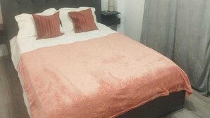 A bedroom with a bed, pillows, a bedside table, a lamp, and a painting on the wall.