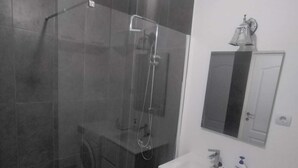 A bathroom with a glass-enclosed shower, a white sink, a mirror, and a washing machine.
