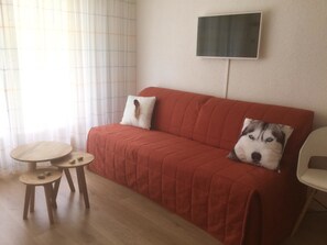 Un sofá rojo con dos almohadones, una mesita de madera con dos sillas y un televisor montado en la pared.