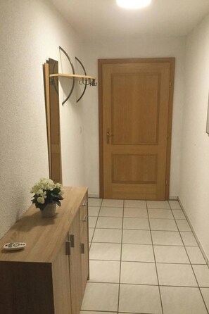 Un pasillo con una puerta de madera, un espejo y una pequeña planta en maceta sobre una consola de madera.