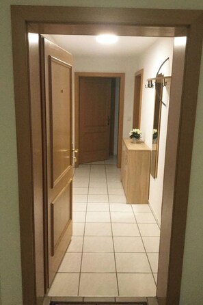 A hallway with a wooden door, a tiled floor, a wooden cabinet, and a mirror. - Les Naturelles B 106 # 5-bed apartment, Dusche und Bad, WC by Interhome (Leukerbad)