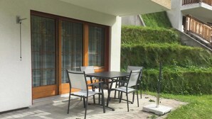 A patio with a table and chairs, a sliding glass door, and a small garden area. - Les Naturelles B 106 # 5-bed apartment, Dusche und Bad, WC by Interhome (Leukerbad)