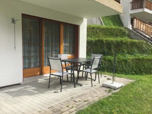 A patio with a table and chairs, a sliding glass door, and a small garden area. - Les Naturelles B 106 # 5-bed apartment, Dusche und Bad, WC by Interhome (Leukerbad)