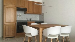 A kitchen with wooden cabinets, a tiled backsplash, a stove, and a dining table with four chairs. - Les Naturelles B 106 # 5-bed apartment, Dusche und Bad, WC by Interhome (Leukerbad)