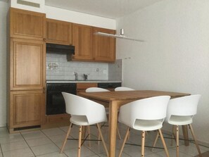 A kitchen with wooden cabinets, a tiled backsplash, a stove, and a dining table with four chairs. - Les Naturelles B 106 # 5-bed apartment, Dusche und Bad, WC by Interhome (Leukerbad)
