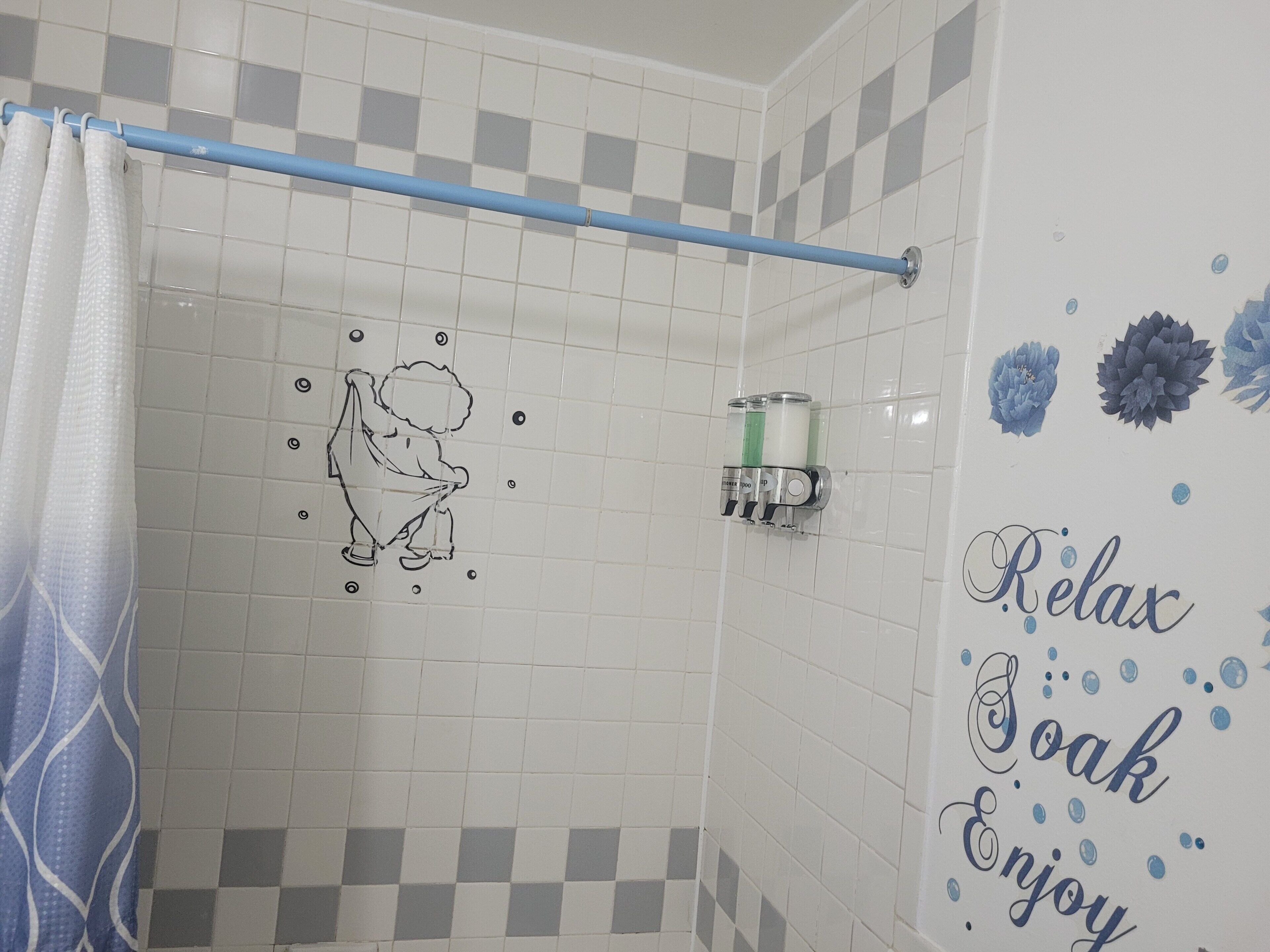 Une douche avec un rideau bleu, un distributeur de savon fixé au mur et un motif décoratif sur les carreaux.