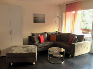 A modern living room with a sectional sofa, a glass coffee table, and a small ottoman. - Edelweiss D 11 # 4-bed apartment, Dusche, WC 4-Bettwohnung, Dusche, WC by Interhome (Leukerbad)