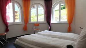 Ett hotellrum med två sängar, en stol och stora fönster med gardiner.
