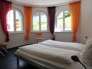 A hotel room with two beds, a chair, and large windows with curtains. - Edelweiss D 11 # 4-bed apartment, Dusche, WC 4-Bettwohnung, Dusche, WC by Interhome (Leukerbad)