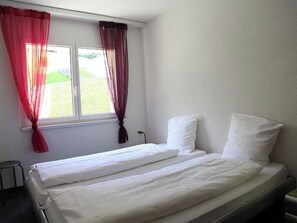 Ein Einzelbett mit weißer Bettwäsche in einem Zimmer mit Fenster und Vorhängen.