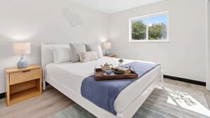 Un dormitorio con cama, mesitas de noche, una ventana y una bandeja con objetos sobre la cama.