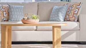 Un sofá con cojines estampados, una mesa tejida y una cesta con piedras y una planta.