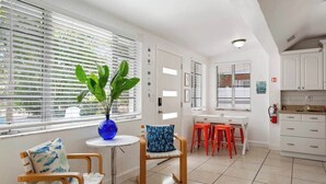 A modern kitchen with white cabinets, a dining area with a table and chairs, and a large window with blinds. - •Cozy•3BR•SRQ•Walk To Ringling•Near Beach•Peacocks (Sarasota)