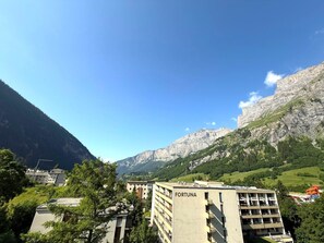 Un edifici de diverses plantes amb el nom 'FORTUNA' a la façana, envoltat de vegetació exuberant i muntanyes al fons.