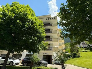 A multi-story building with a 'ROYAL' sign, parked cars, and lush greenery. - Royal 51 # 4-bed apartment, Bad, WC 4-Bettwohnung, Bad, WC by Interhome (Leukerbad)