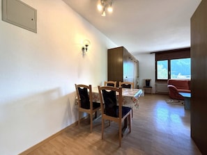 A dining area with a table and chairs, a wooden cabinet, and a window with a view. - Royal 51 # 4-bed apartment, Bad, WC 4-Bettwohnung, Bad, WC by Interhome (Leukerbad)