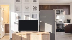 Une cuisine moderne équipée d’un téléviseur à écran plat, d’appareils électroménagers en acier inoxydable et d’un mur décoré de tableaux encadrés.