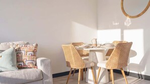 Un coin repas avec des chaises en osier, une table ronde et un canapé blanc agrémenté de coussins à motifs.