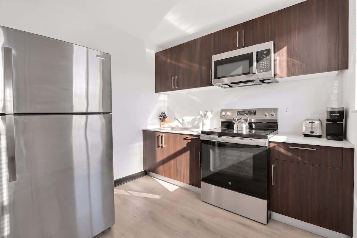 A modern kitchen with stainless steel appliances, wooden cabinets, and a countertop with a kettle and toaster.